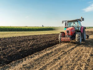 Farmer plowing stubble field with red tractor